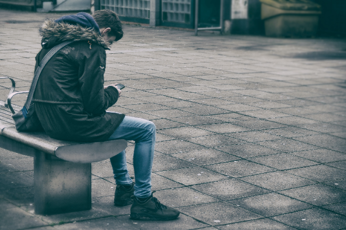 This is an image of a boy looking at his phone while sitting on a bench outside